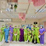 Grupo de enfermeiras em uniformes coloridos reunido dentro de uma ala hospitalar.