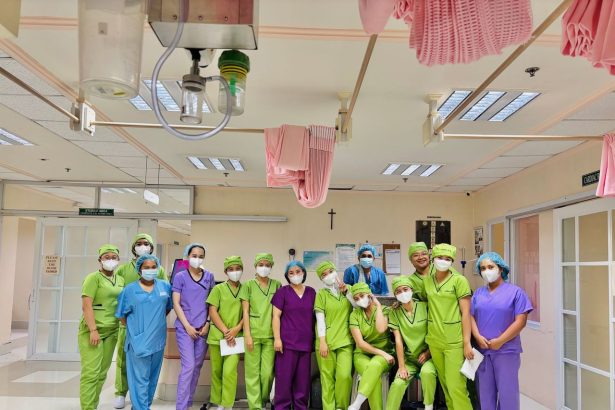 Grupo de enfermeiras em uniformes coloridos reunido dentro de uma ala hospitalar.