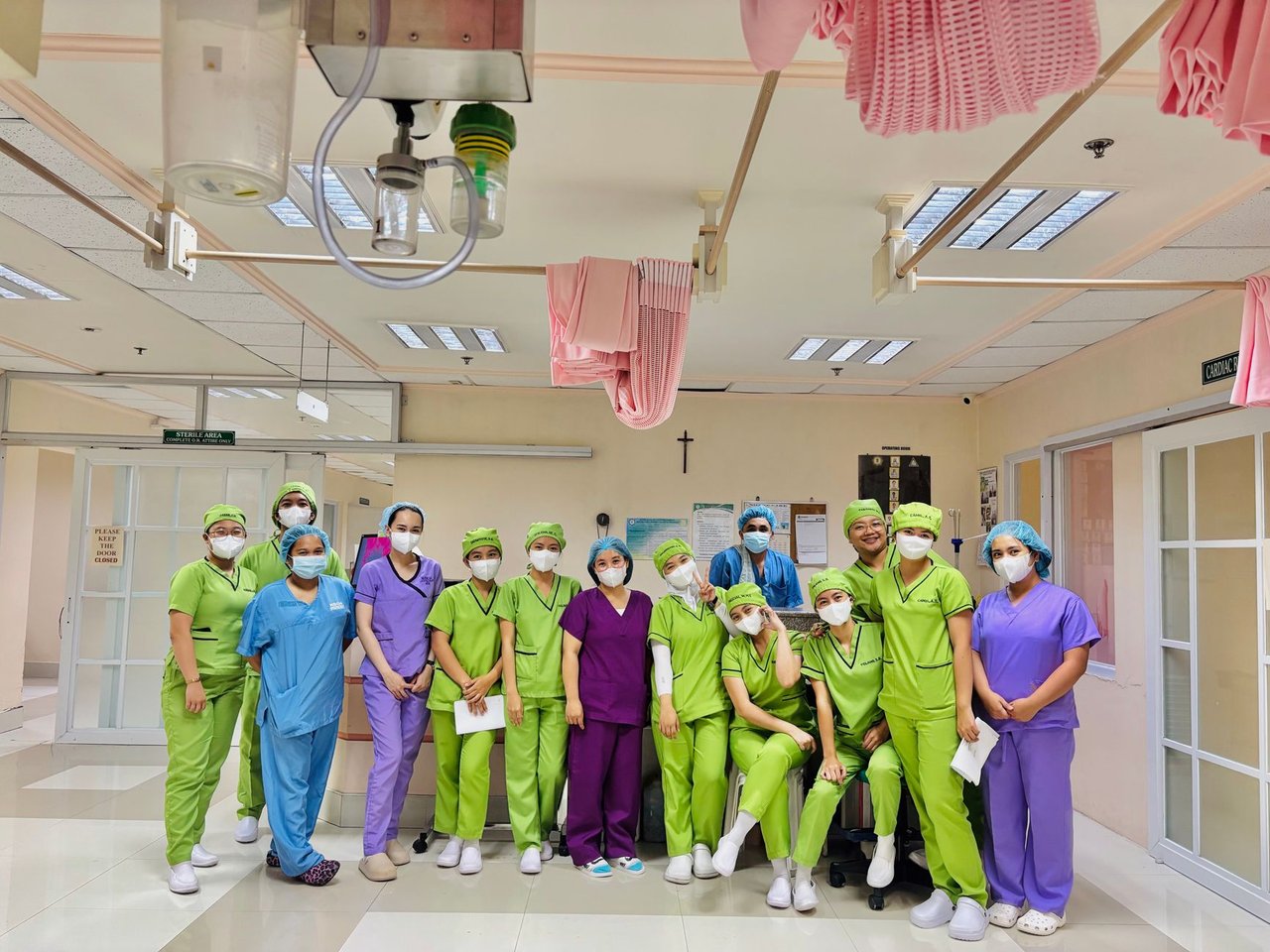 Grupo de enfermeiras em uniformes coloridos reunido dentro de uma ala hospitalar.