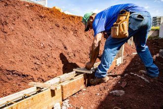 Trabalhador da construção civil atua na fundação de uma obra ao ar livre.