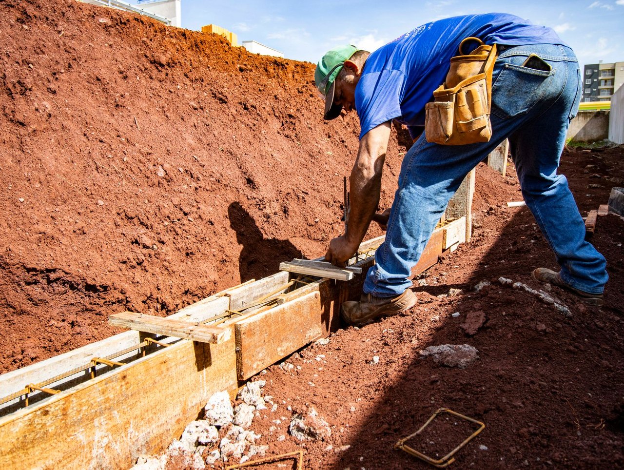 Trabalhador da construção civil atua na fundação de uma obra ao ar livre.