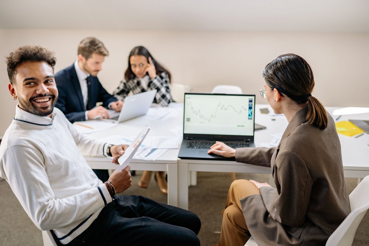 Grupo de profissionais analisa gráficos e dados em uma reunião de trabalho com uso de tecnologia.